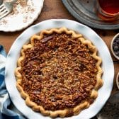 Overhead shot of a baked chocolate pecan pie in a white pie dish on a wooden table.