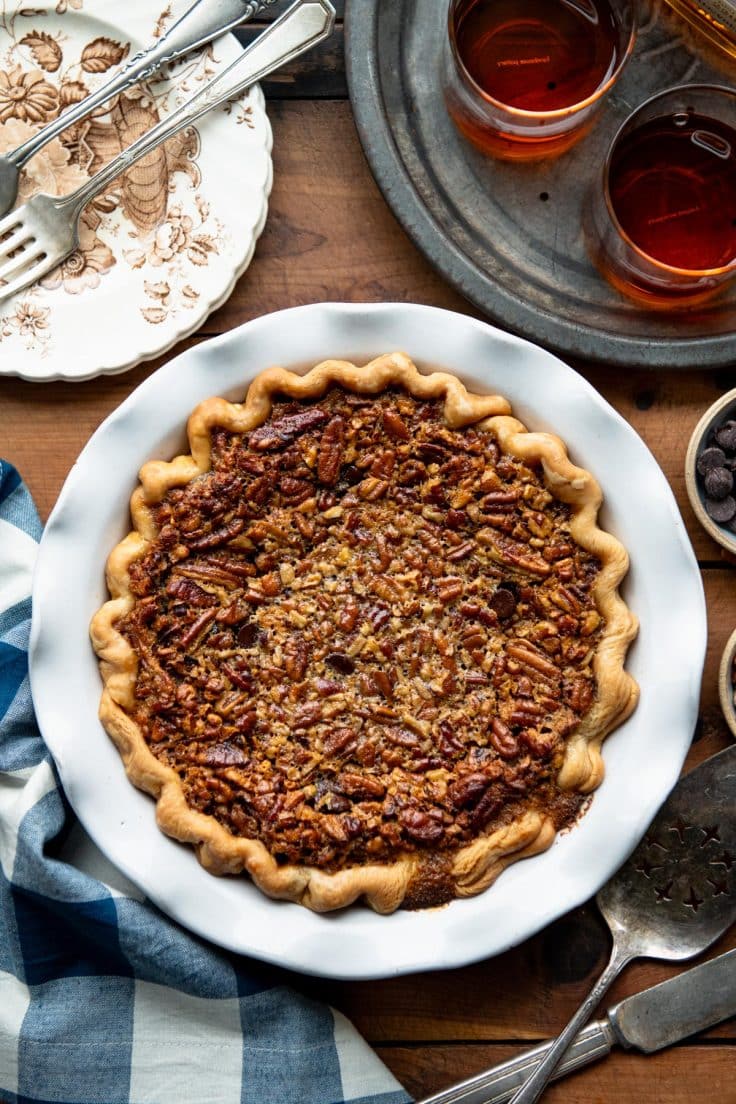 Overhead shot of a baked chocolate pecan pie in a white pie dish on a wooden table.