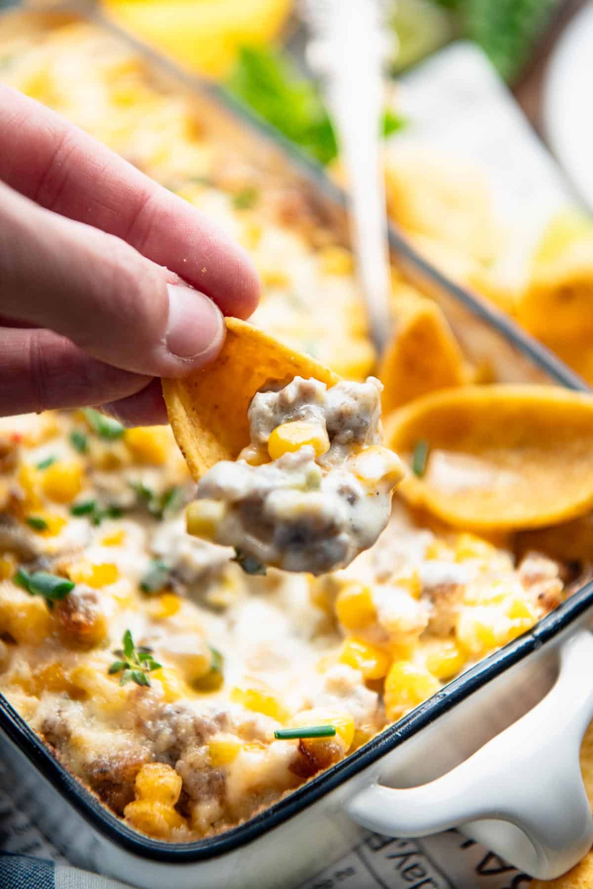 Hand holding a chip with corn dip.