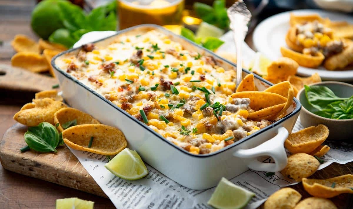 Horizontal image of a white dish full of hot corn dip with sausage.