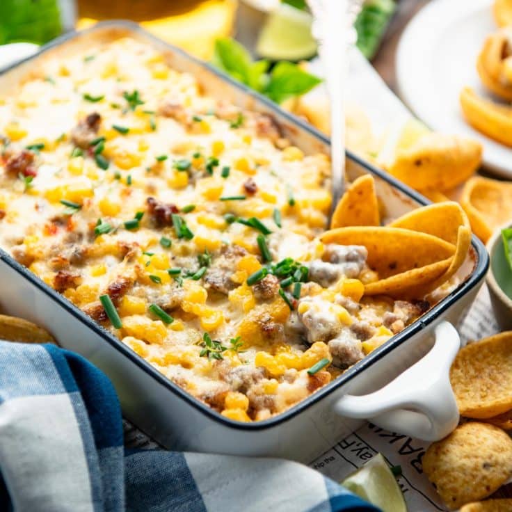 Square close up side shot of corn chips with a pan of hot sausage dip.