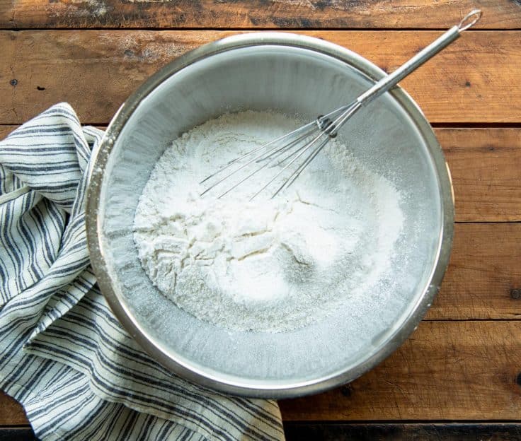 Whisking together dry ingredients in a metal mixing bowl.