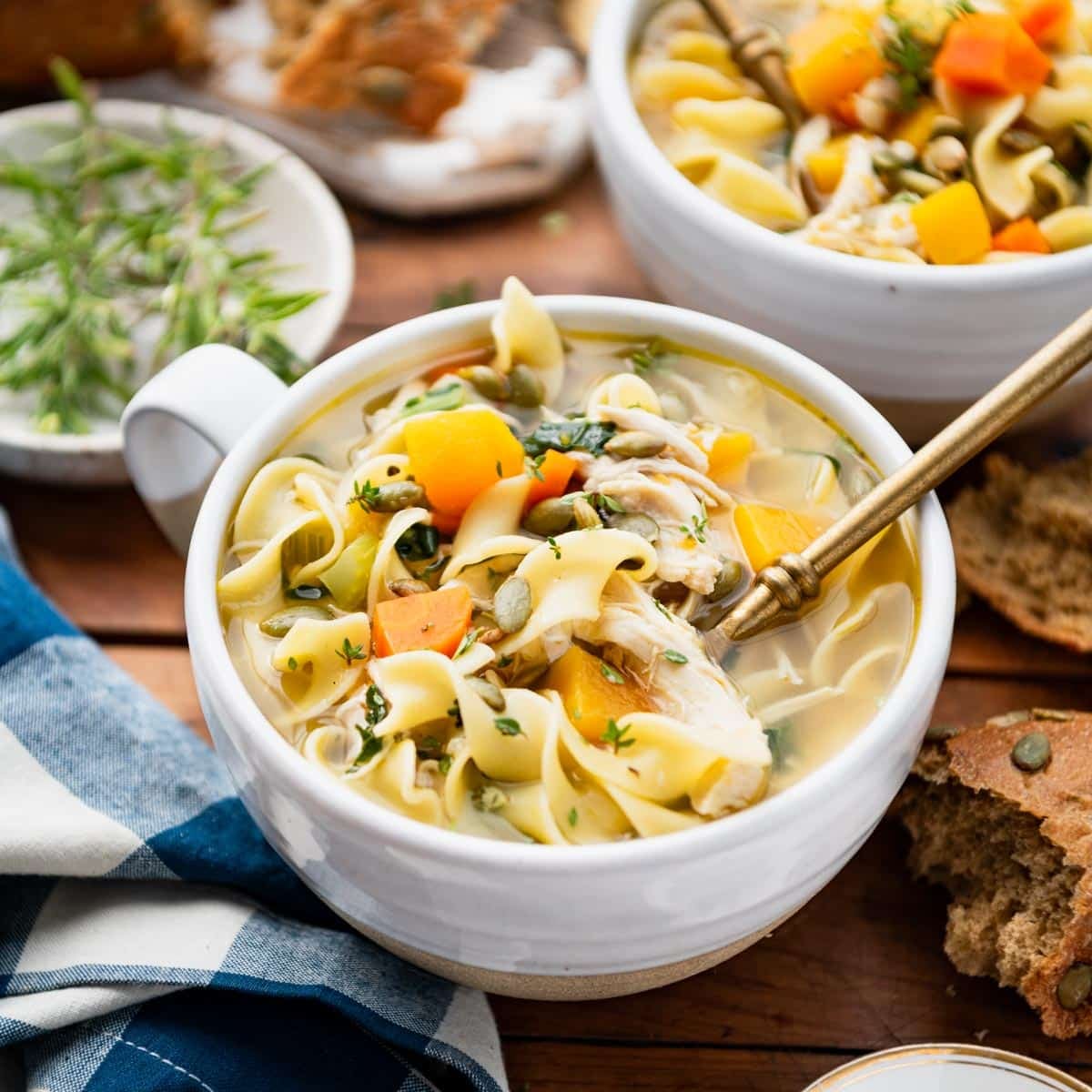 Square side shot of a white mug full of autumn harvest chicken noodle soup.