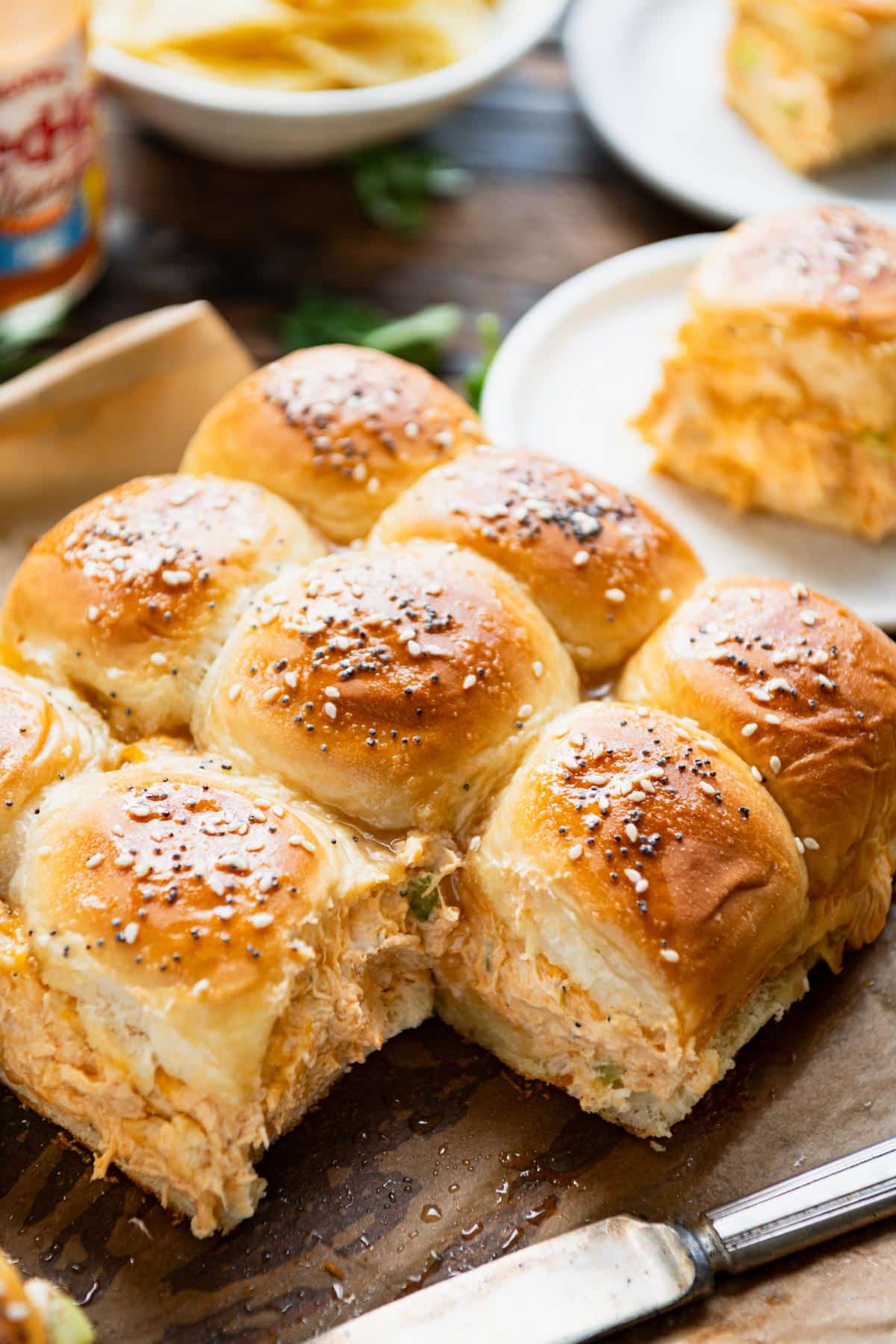 Tray of the best buffalo chicken sliders recipe served on a wooden table with potato chips and salad.