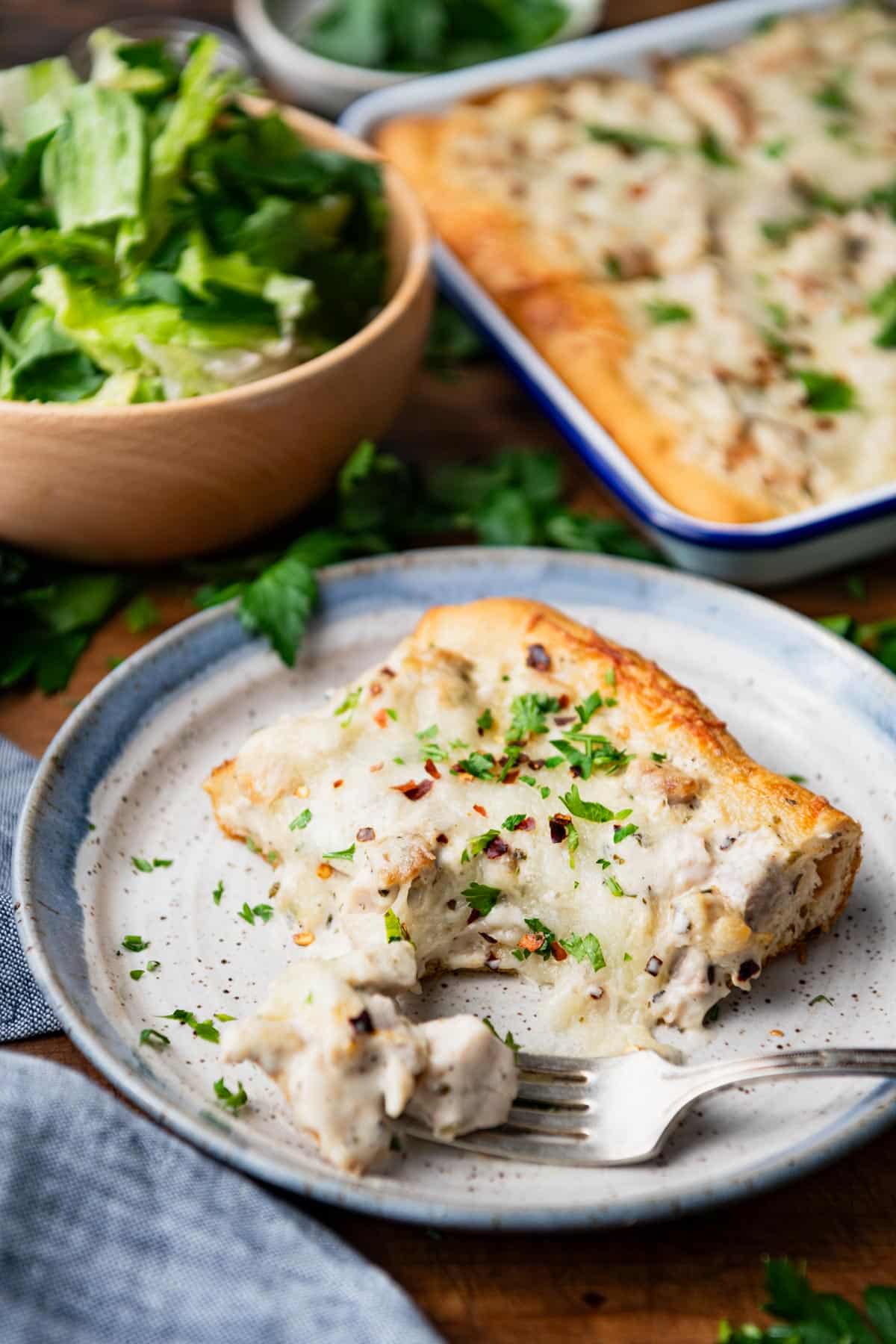 Bite of chicken alfredo crescent roll casserole on a fork on a plate.