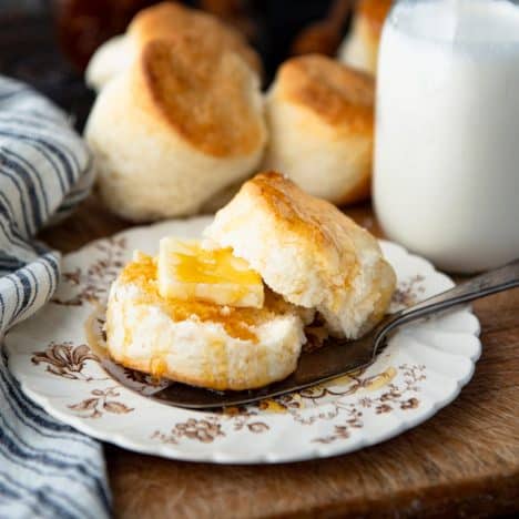 Square side shot of a plate of heavy whipping cream biscuits on a vintage plate with honey and butter.