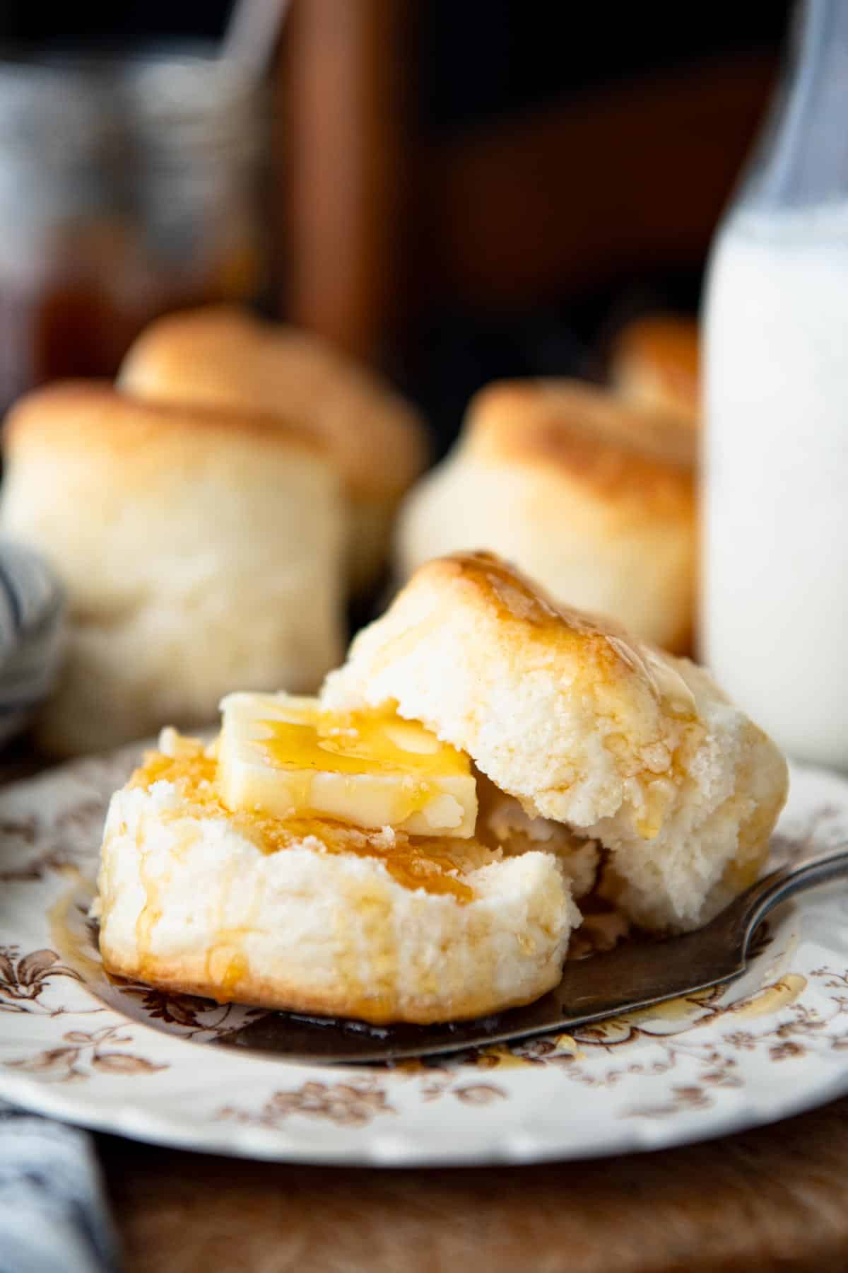 A heavy cream biscuit split in half on a plate and served with butter and honey.