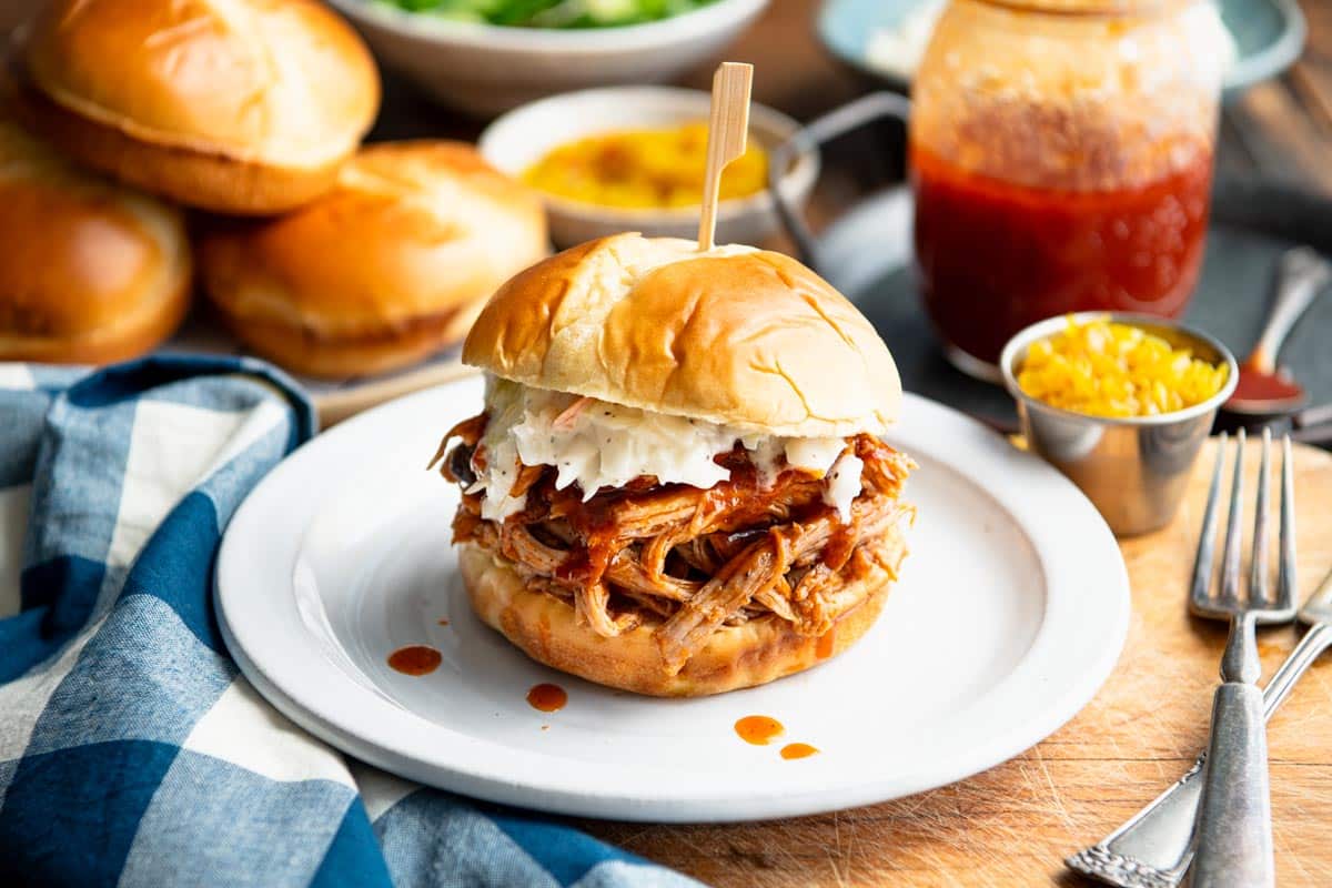 Horizontal shot of slow cooker pulled pork sandwich with maple bbq sauce on a white plate.