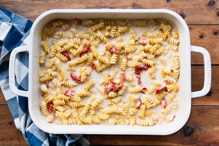 Process shot showing how to make sun dried tomato pasta in a white baking dish.