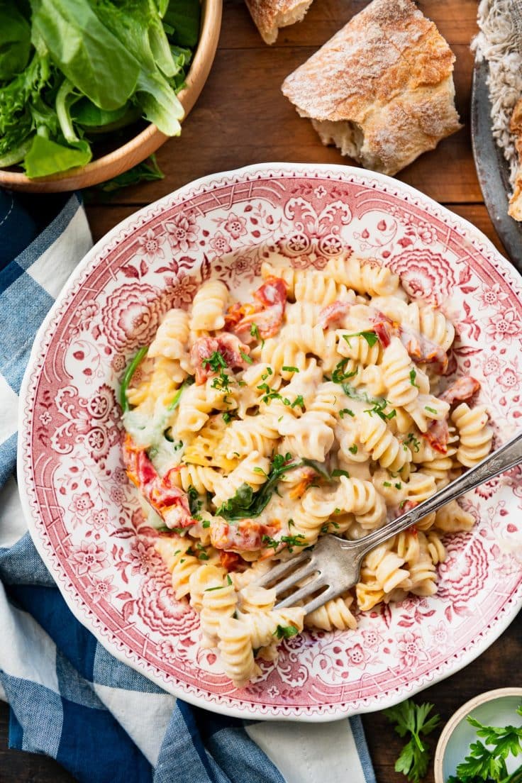 Close overhead image of a red and white bowl full of dump and bake sun dried tomato pasta.