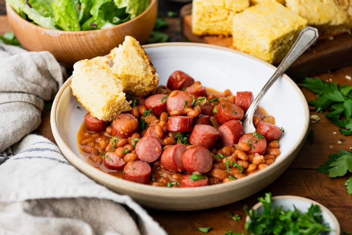 Horizontal side shot of franks and beans in a white bowl with a side of cornbread.
