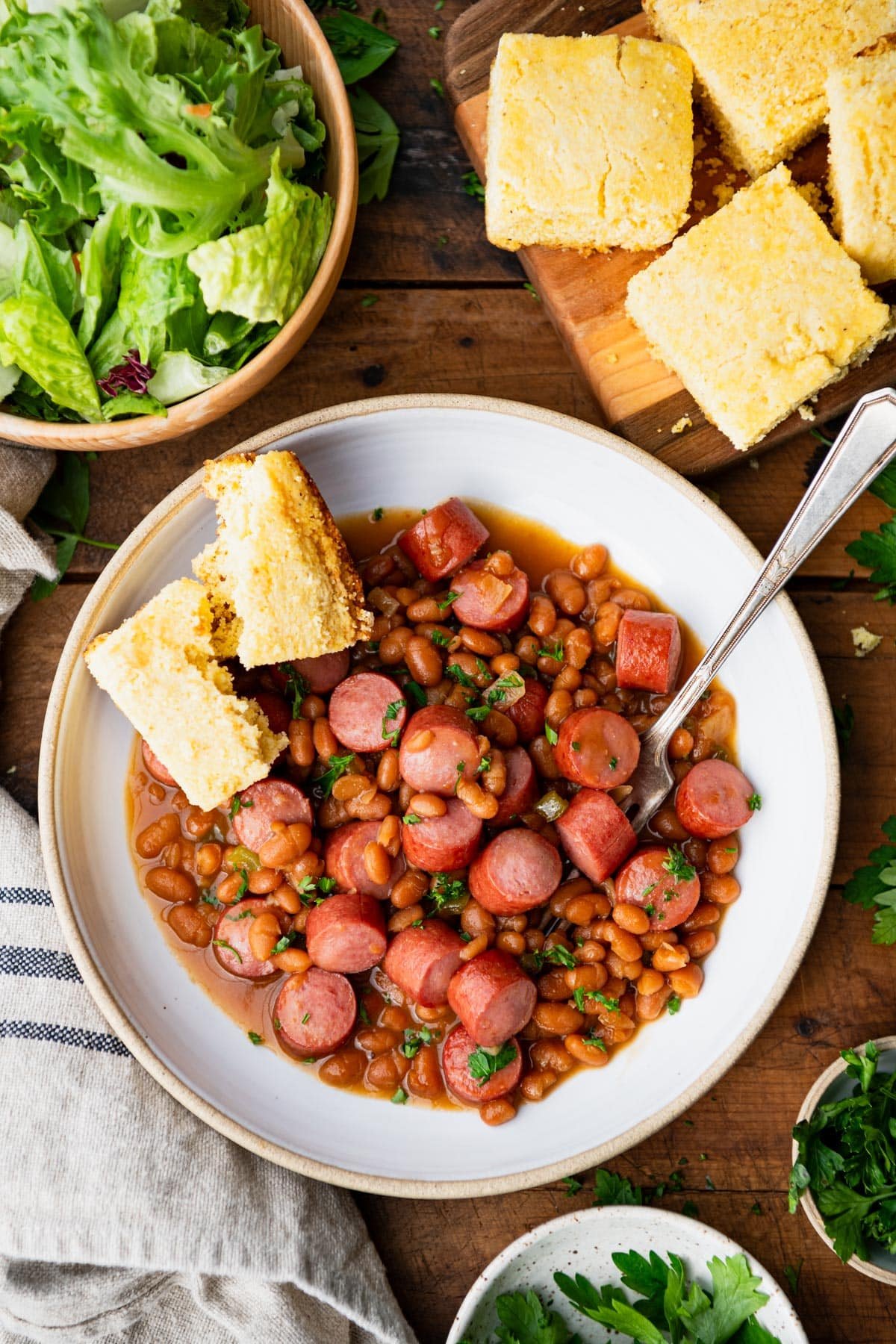 Overhead shot of a bowl of beanee weenees on a table with a side of cornbread.