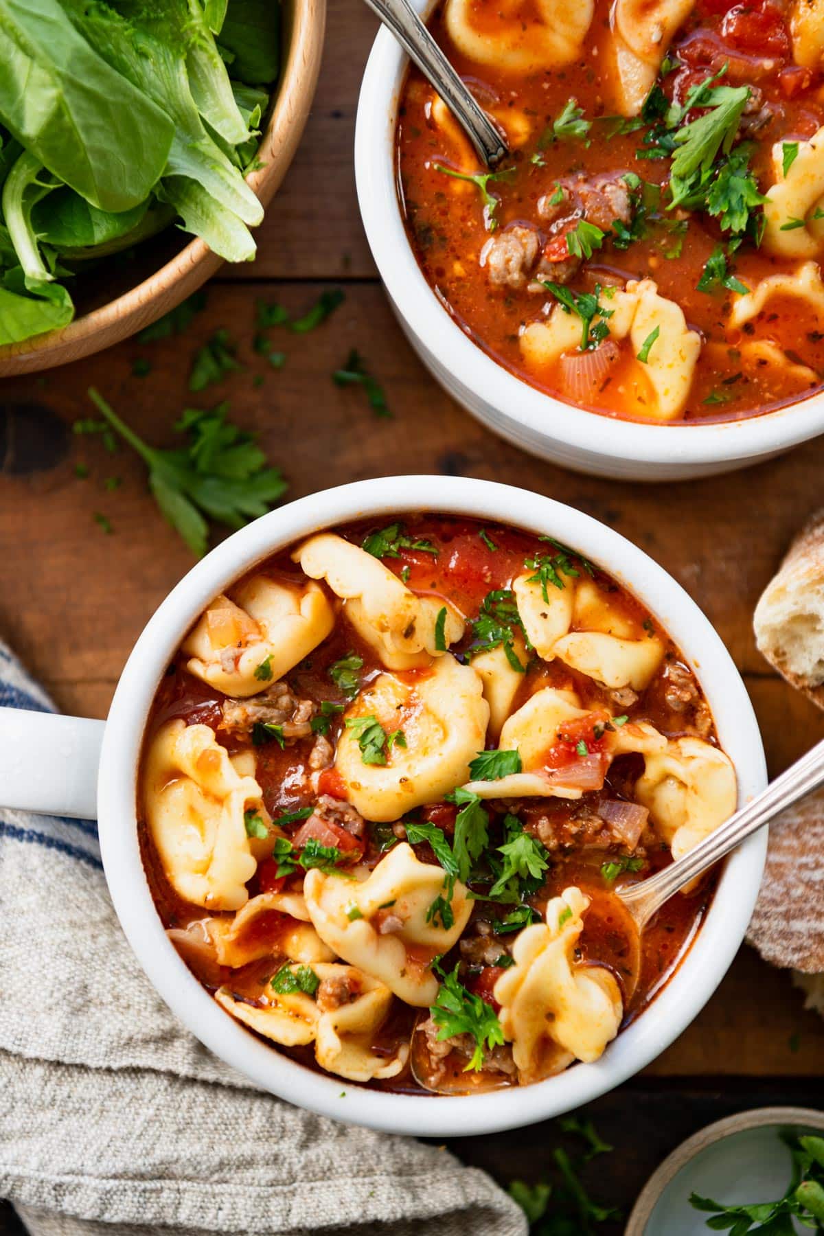 Close overhead image of tortellini soup with sausage in a white bowl.
