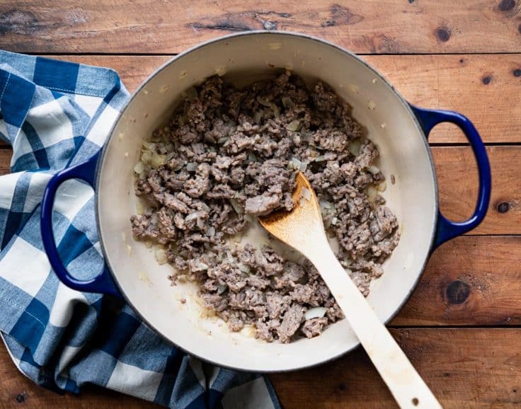 Process shot of browning Italian sausage with onion in a Dutch oven.