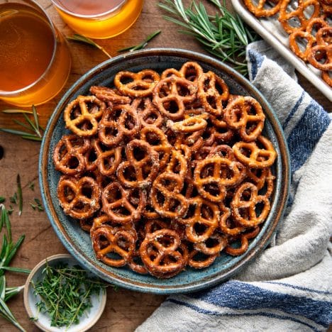 Square overhead image of ranch pretzels in a bowl on a wooden table with a side of beer.