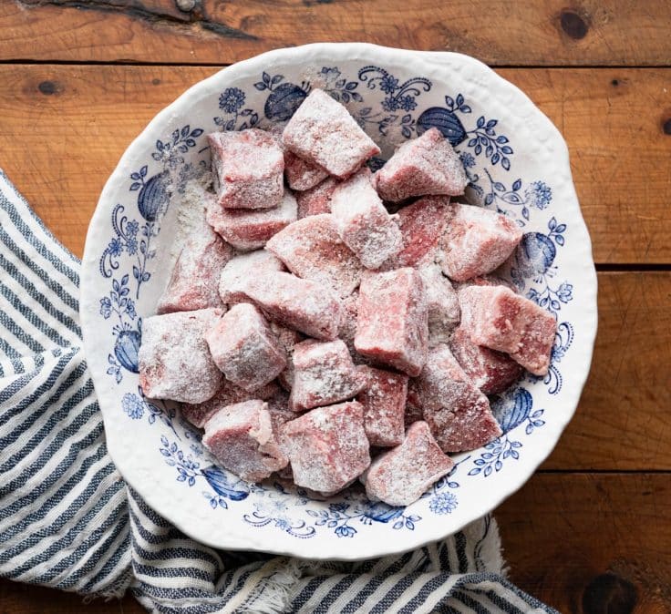 Raw beef tips in a bowl and coated in flour.
