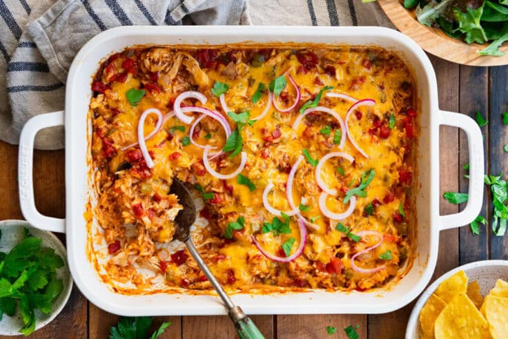 Horizontal overhead shot of a serving spoon in a pan of baked chicken fajita casserole.