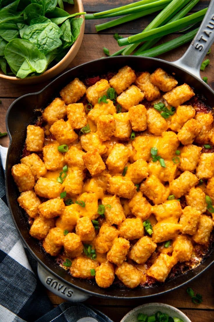 Close overhead shot of cheeseburger tater tot casserole on a wooden table with a salad.