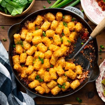 Square overhead image of cheeseburger tater tot casserole in a cast iron pan.