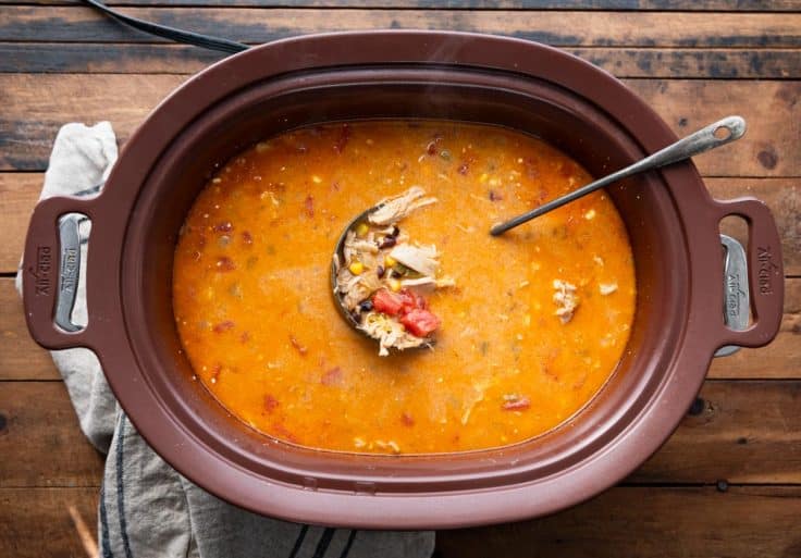 A ladle in a slow cooker full of the best chicken enchilada soup recipe.