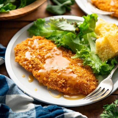 Square side shot of a honey butter chicken breast on a plate with salad and cornbread.