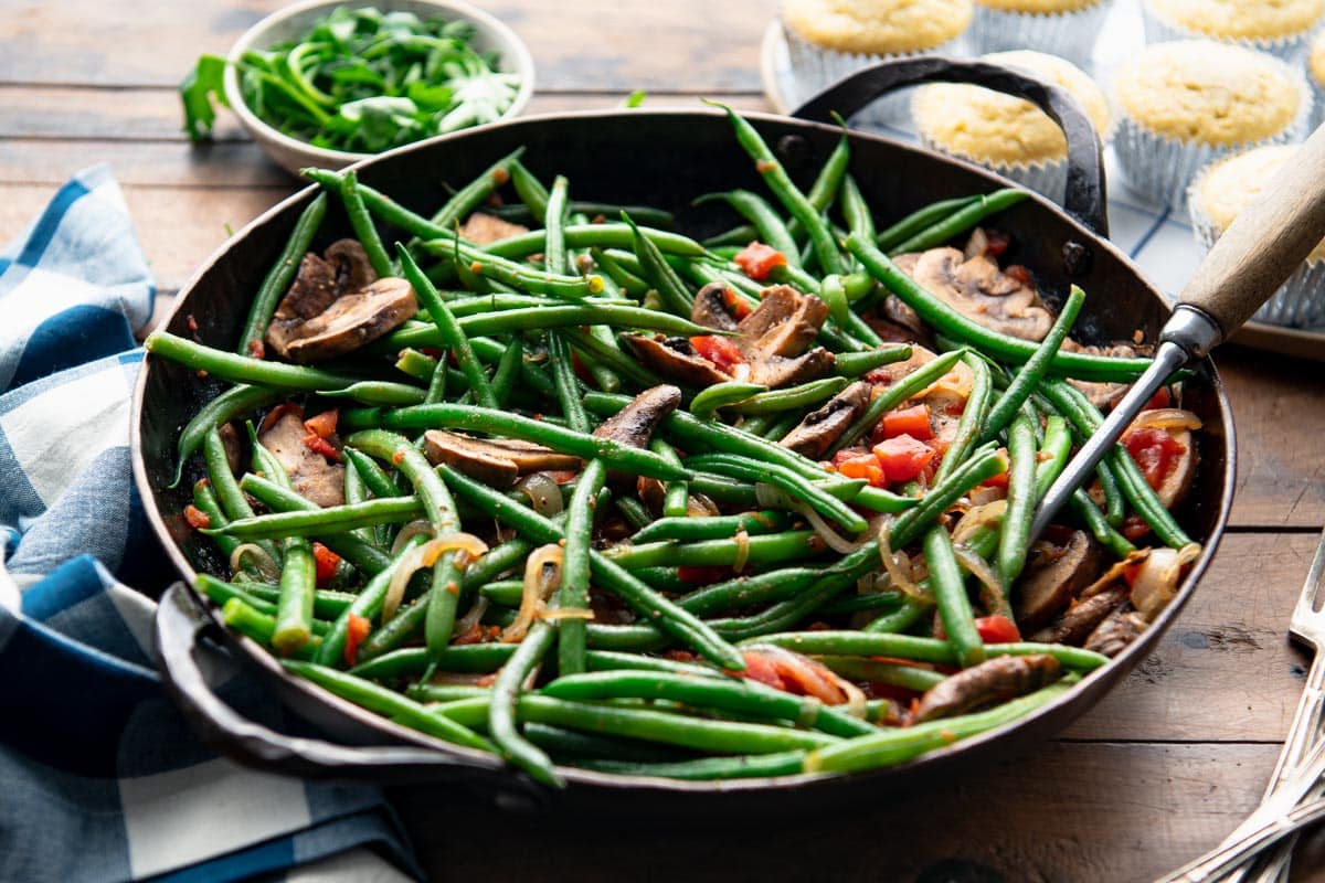 Horizontal side shot of a skillet of green beans with mushrooms and onions.