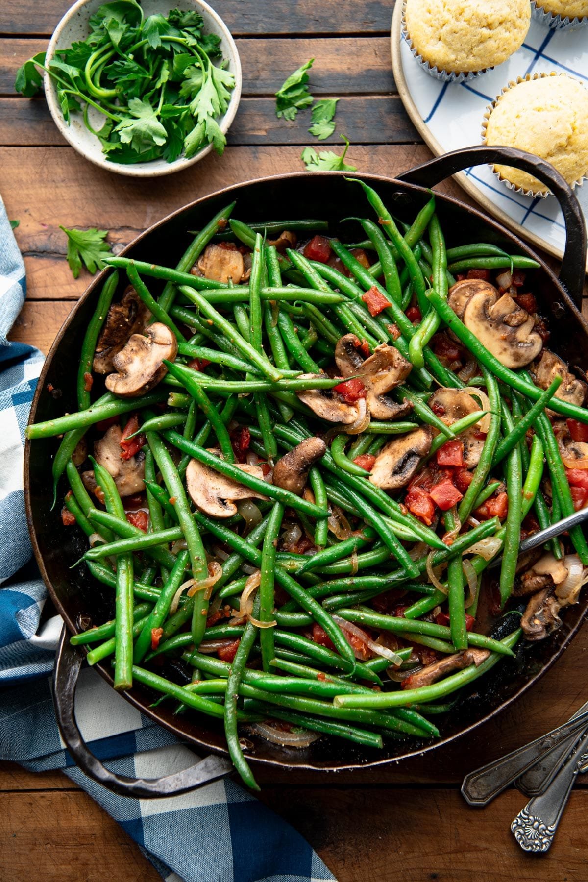 Overhead shot of green beans with mushrooms and onions on a wooden table.
