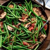 Close overhead shot of green beans with mushrooms and onions in a pan.