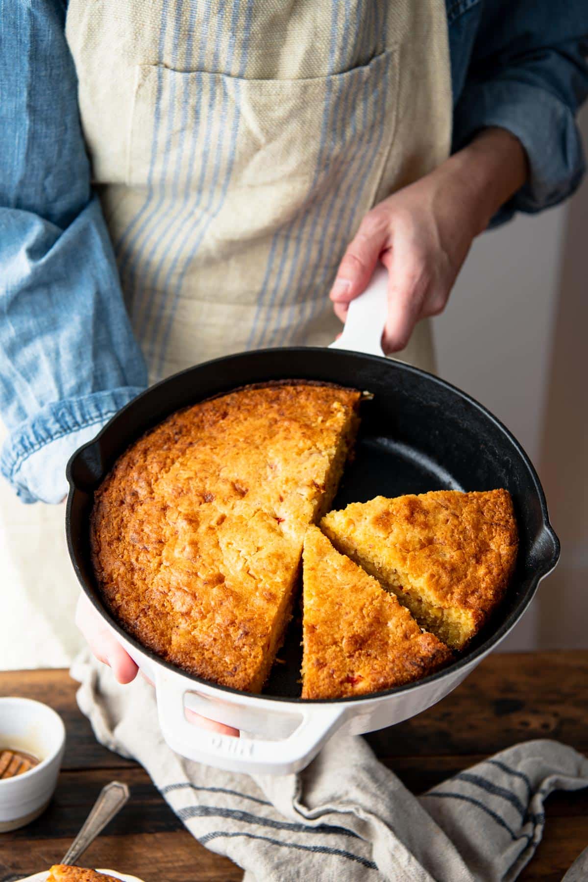 Hands holding a moist cornbread recipe baked in a cast iron skillet.