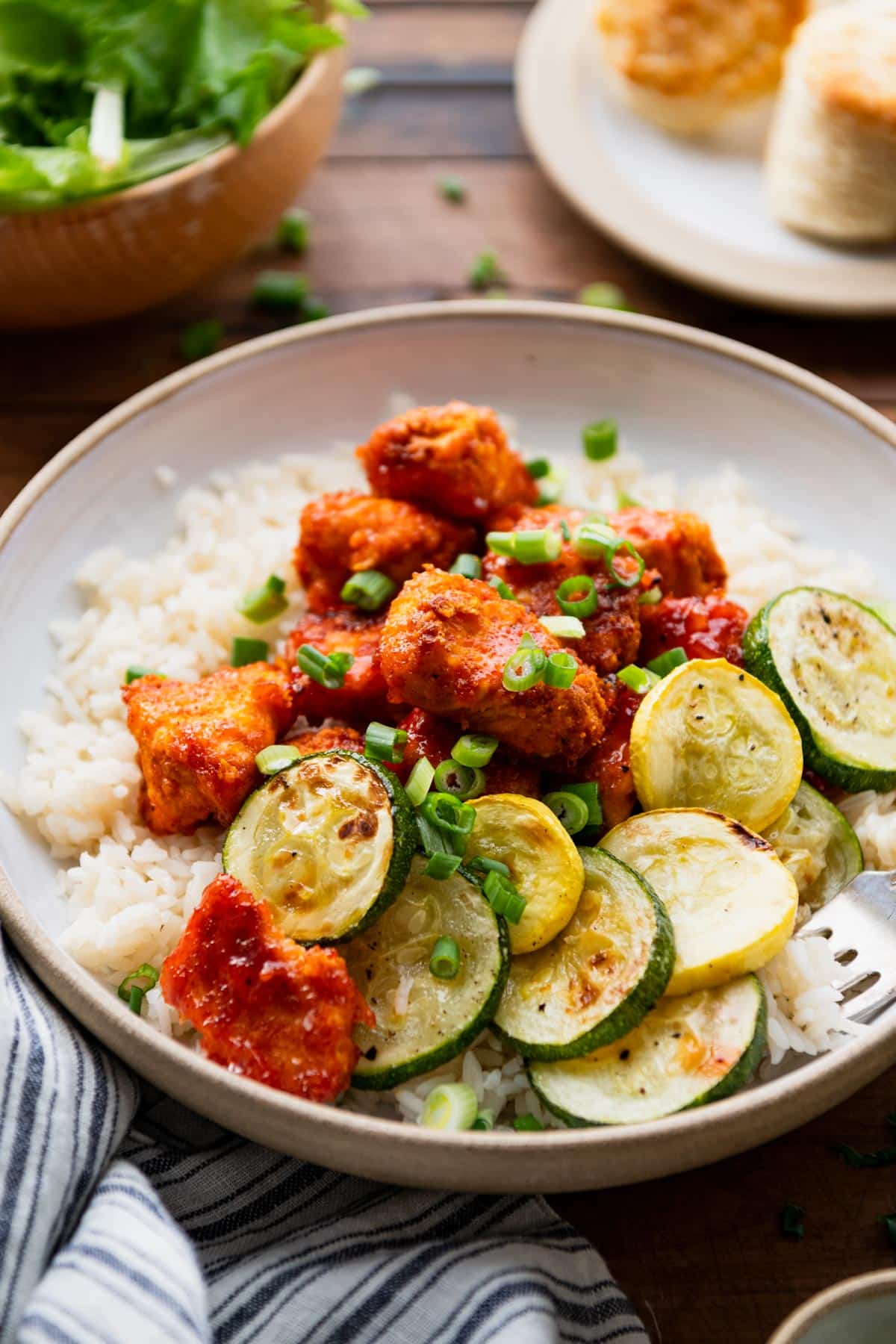 Close up side shot of orange marmalade chicken with zucchini and rice in a white bowl.
