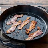 Bacon frying in a cast iron skillet.