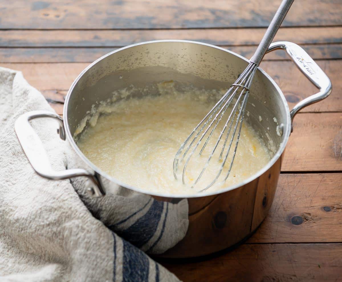 Whisking cheese grits in a pot.