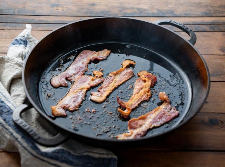 Bacon frying in a cast iron skillet.