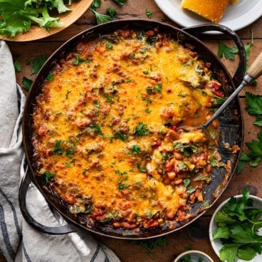 Square overhead shot of a pan of bean casserole on a wooden dinner table.