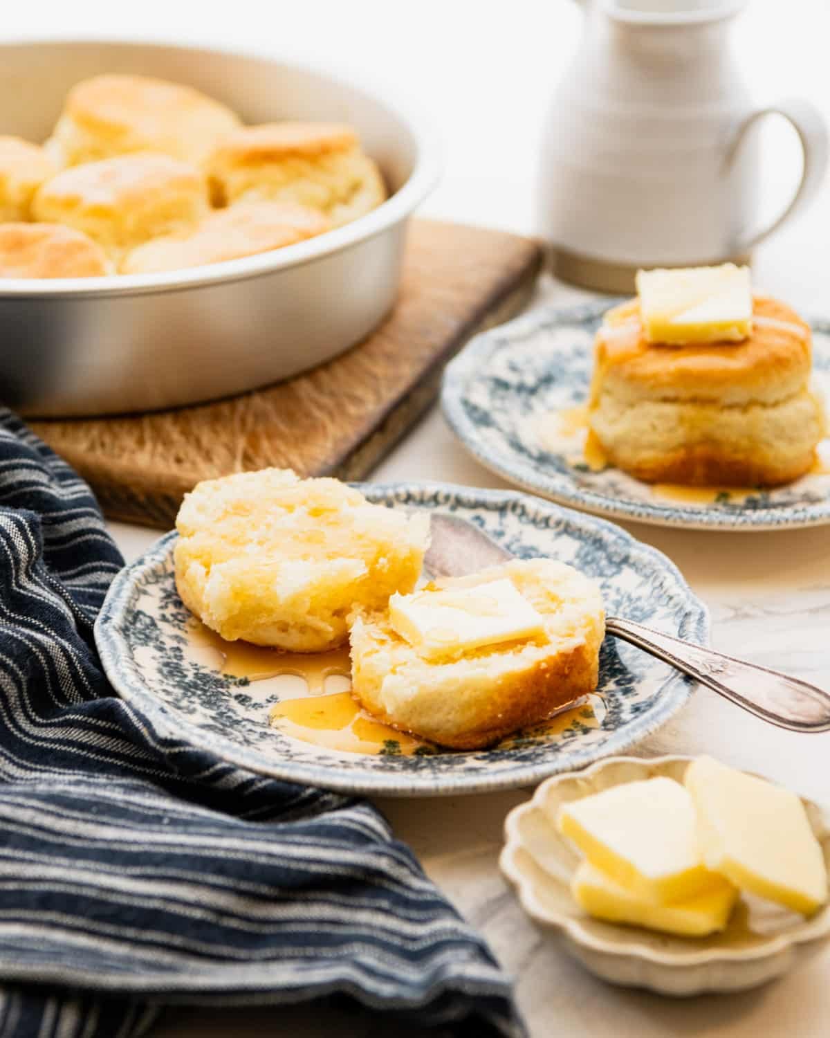 Side shot of split cream biscuits on blue and white plates with butter and honey.