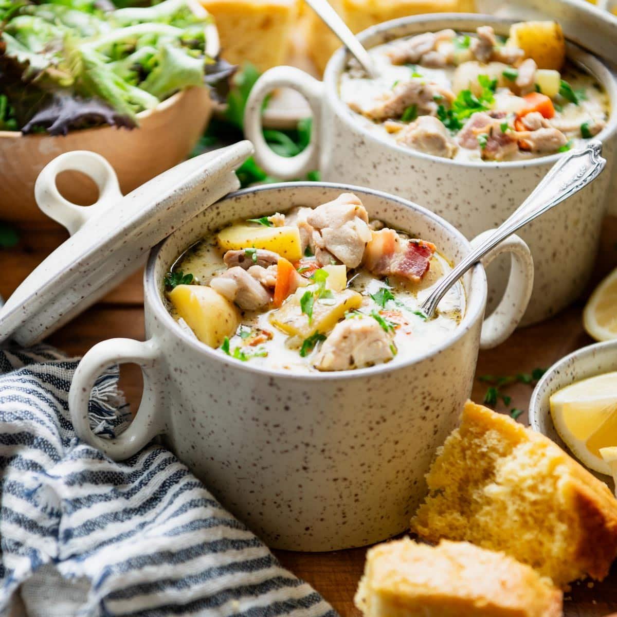 Square side image of a bowl of chicken potato soup with cornbread and salad on the side.