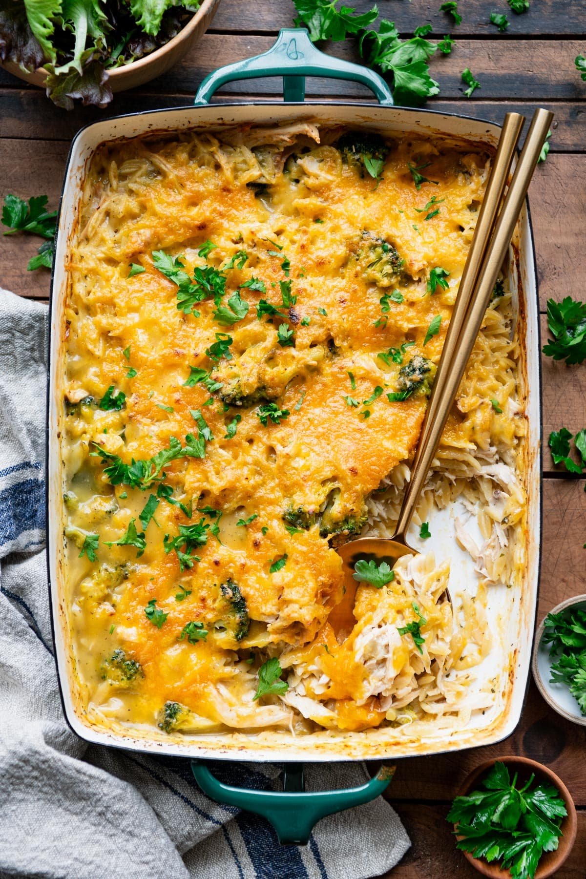Overhead image of a cheesy creamy chicken orzo casserole on a wooden dinner table.