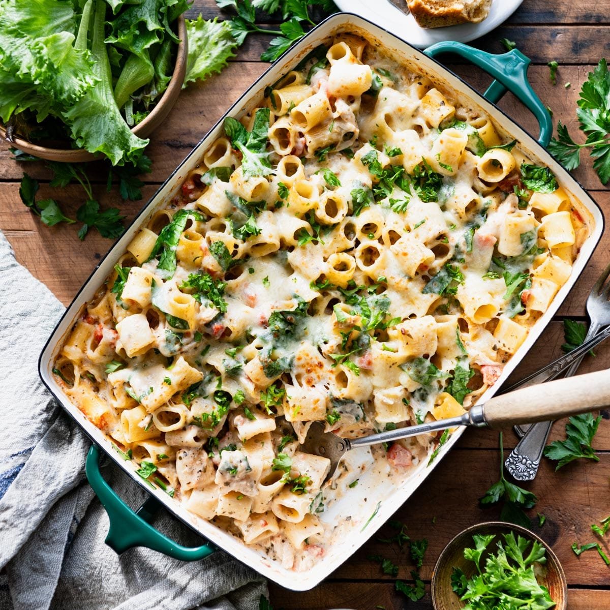 Square overhead image of chicken pesto alfredo pasta bake on a wooden dinner table.