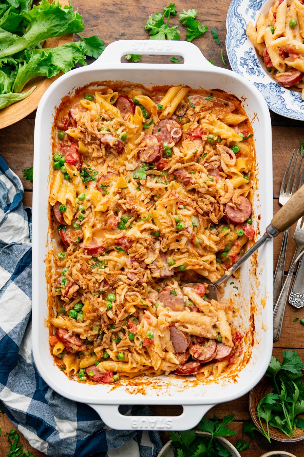 Overhead image of a white baking dish full of smoked sausage pasta casserole on a dinner table.