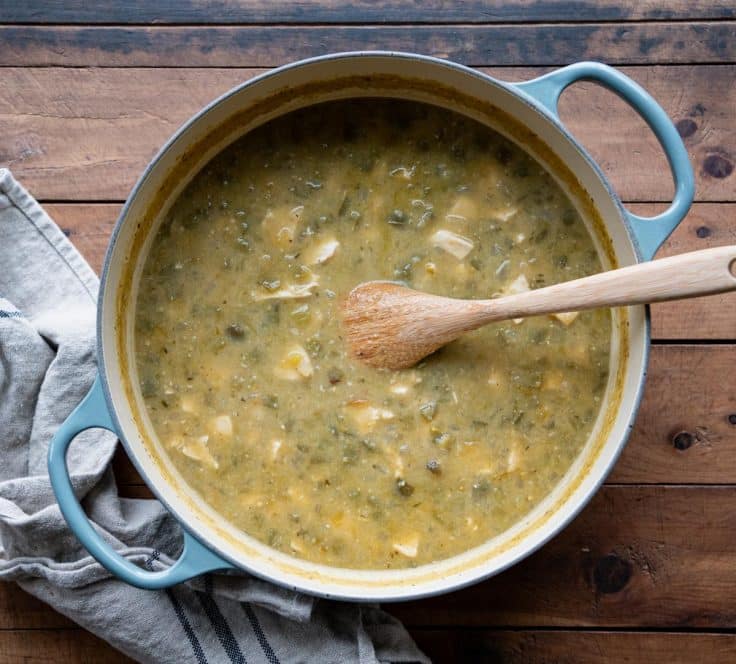 Wooden spoon stirring a Dutch oven full of green chicken chili.