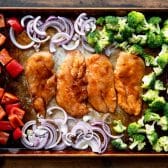 Arranging chicken breast and vegetables on a baking sheet.