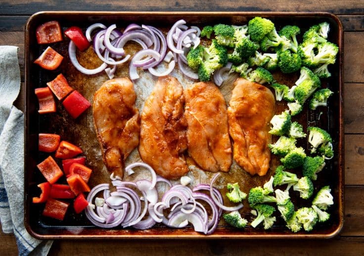 Arranging chicken breast and vegetables on a baking sheet.