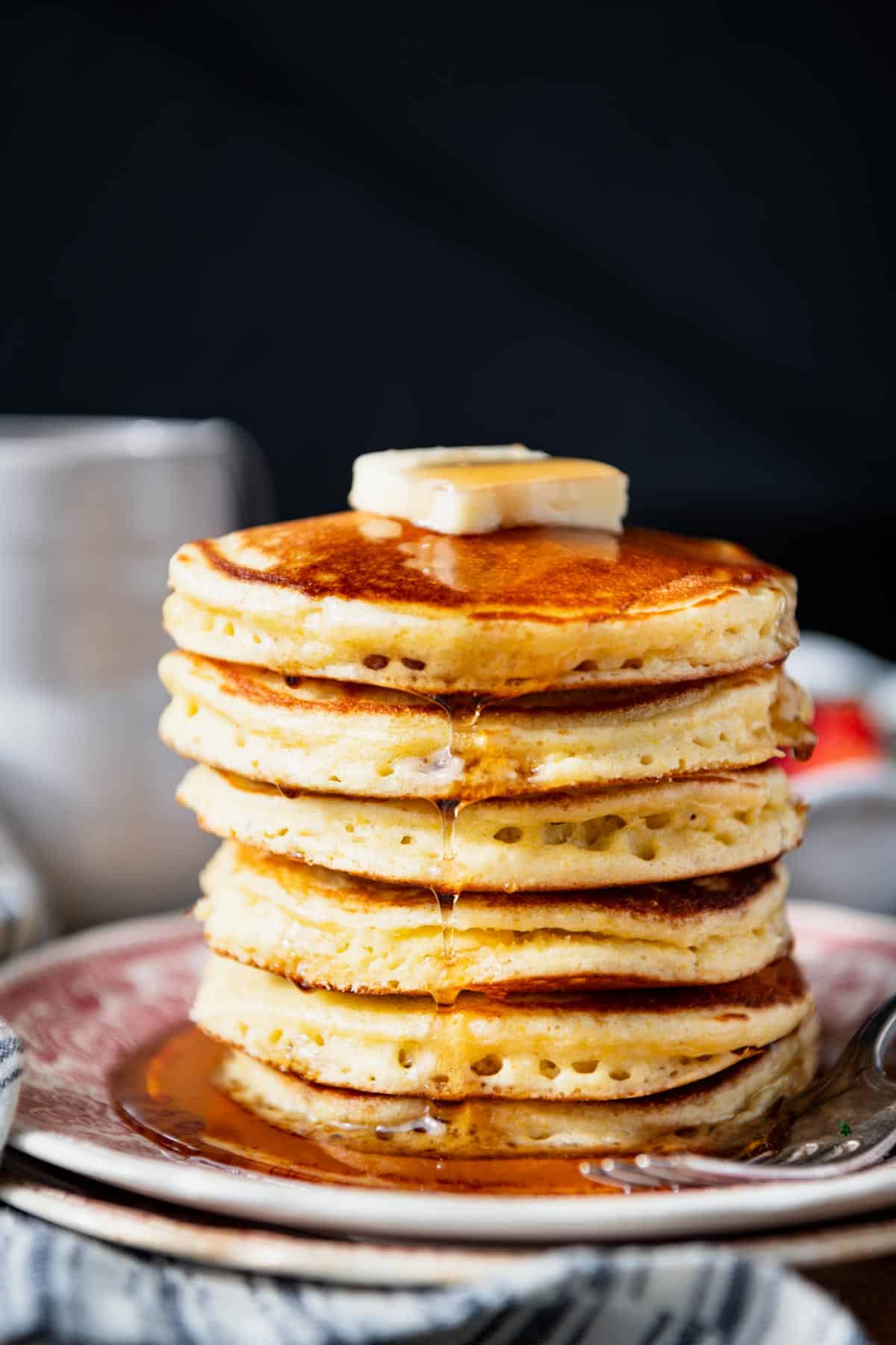 Close up side shot of a stack of Jiffy cornmeal pancakes on a read and white plate.
