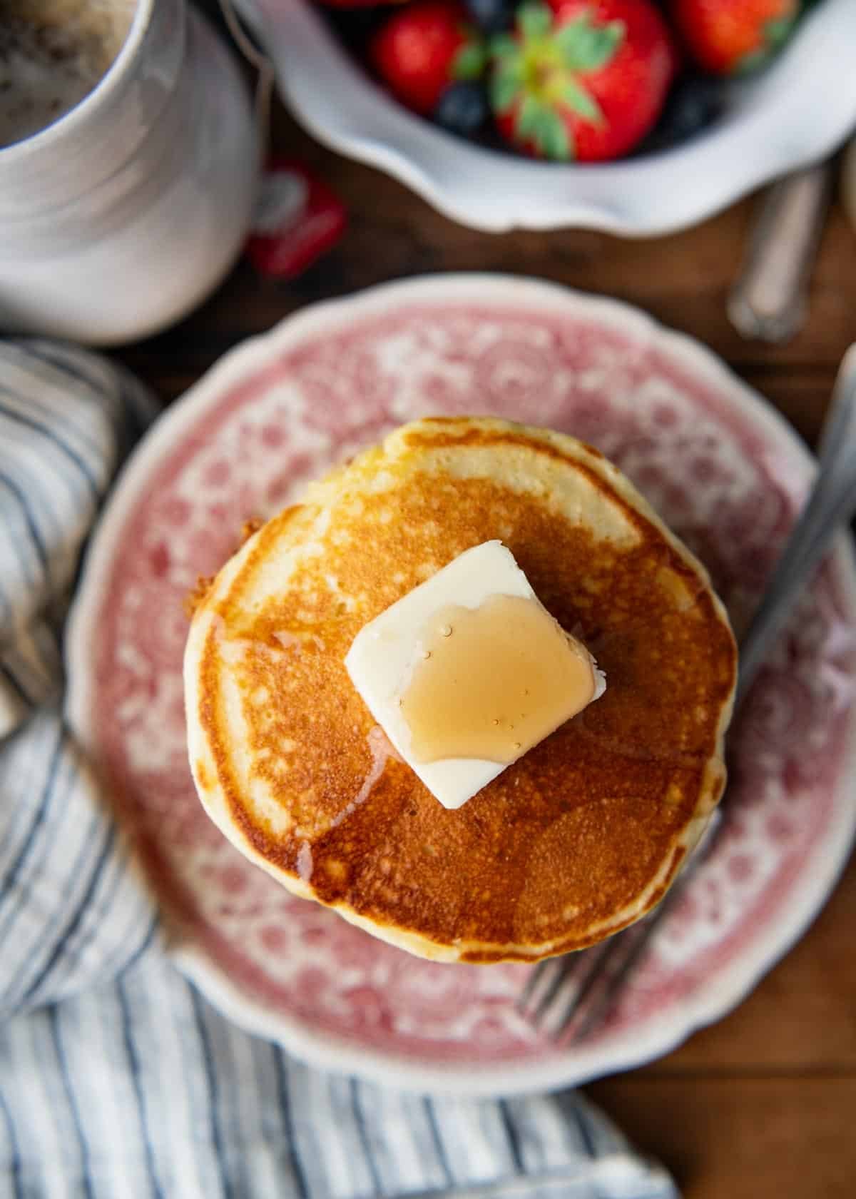 Overhead shot of butter and syrup on a plate of Jiffy cornmeal pancakes.
