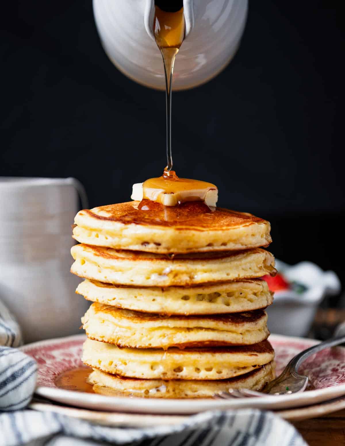 Pouring syrup over a stack of Jiffy cornmeal pancakes.