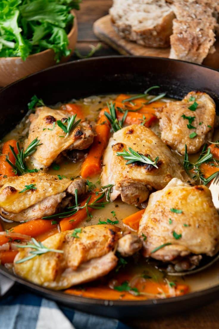 Close up side shot of braised chicken thighs in a cast iron skillet.