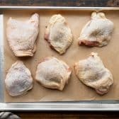 Bone in skin on chicken thighs on a rimmed baking sheet.