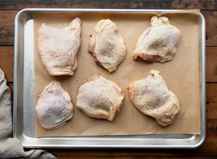 Bone in skin on chicken thighs on a rimmed baking sheet.