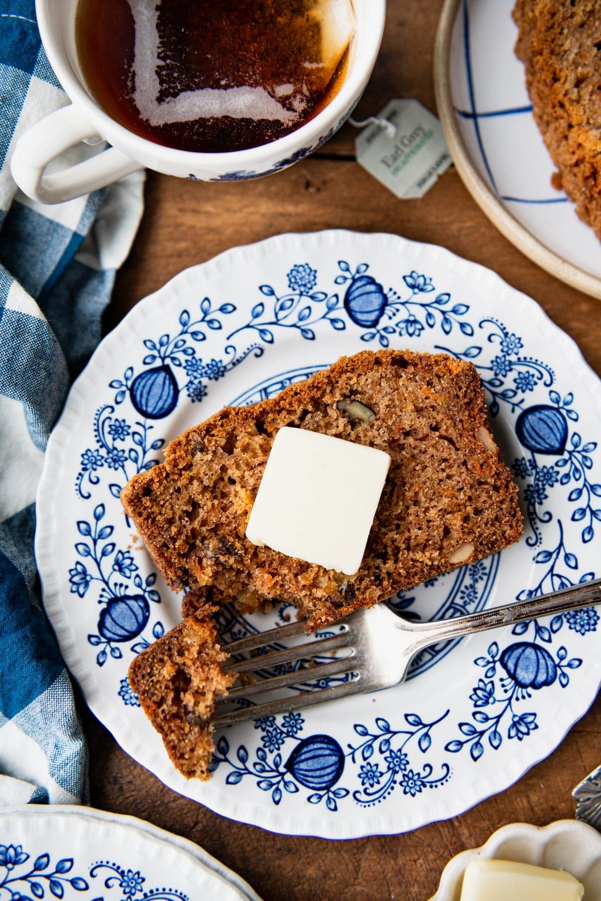 Close overhead shot of a slice of carrot cake loaf on a blue and white plate with butter.