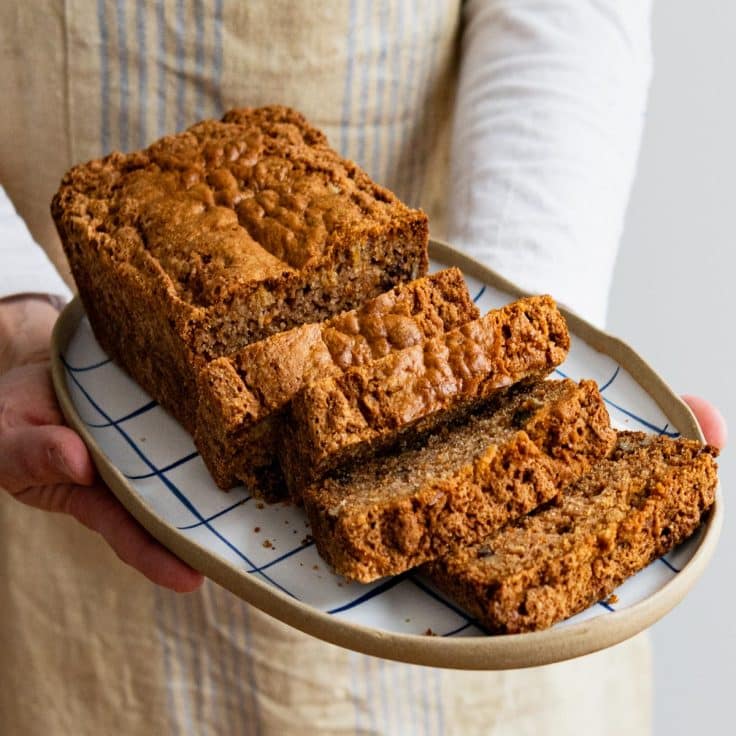 Hands holding a loaf of carrot bread on a serving tray.